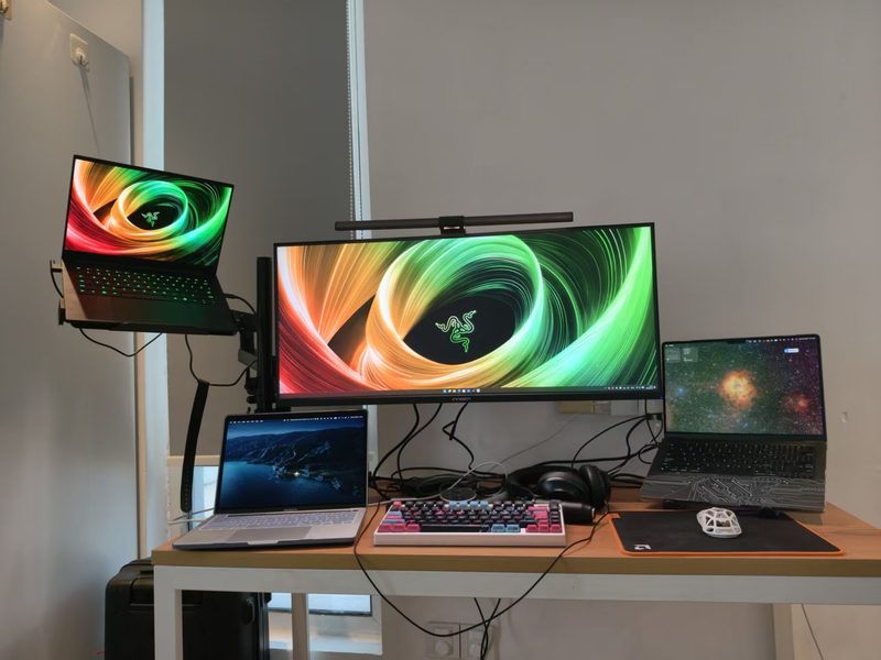 Home desk with a Razer laptop on an arm and an ultrawide monitor