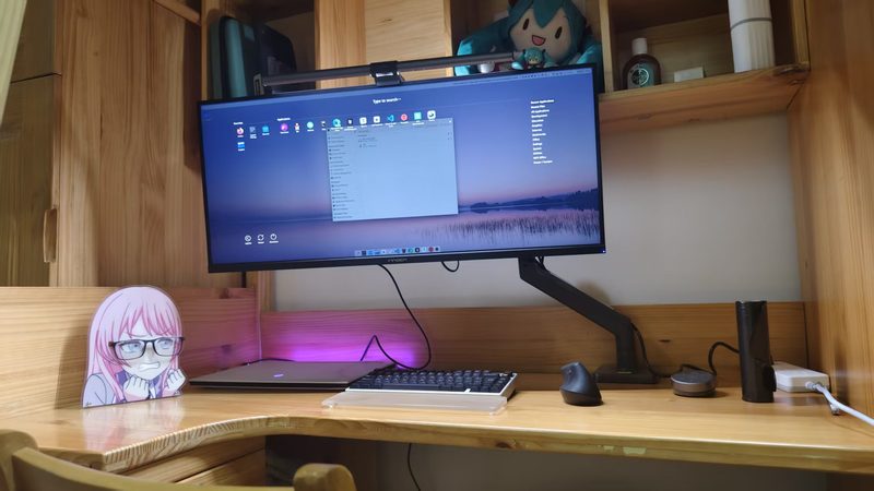 Home desk with a monitor on an arm and a Miku plush on the shelf