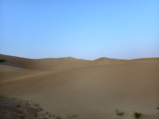 Sand dunes at dusk with tiny figures on the ridge